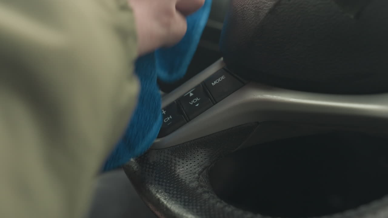 fair skinned person cleaning steering wheel inside car cabin using blue microfibre cloth wiping leather for detail maintenance and hygiene close up shot capturing hand motion and interior focus