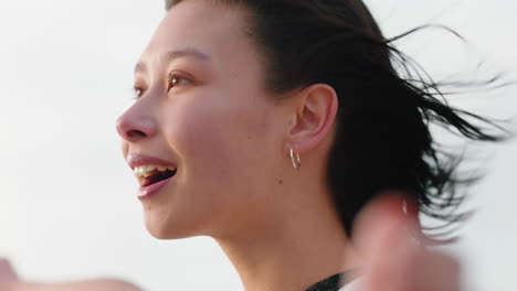 portrait of happy asian woman enjoying freedom arms raised feeling joy on beach at sunset exploring wanderlust with wind blowing hair