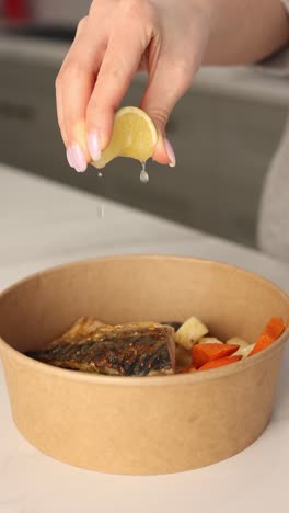 mujer exprimiendo jugo de limón sobre pescado a la parrilla en un recipiente para llevar