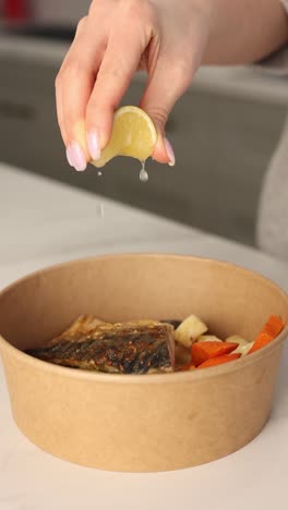 woman squeezing lemon juice over grilled fish in a takeout container