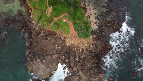 aerial drone top view over scenic tropical pigeon island with lush green trees and ocean waves on rocky beach shore in sri lanka