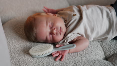 lovely cute newborn baby with blond hair lies sleeping. a hairbrush lies in the hand of a kid. close up.