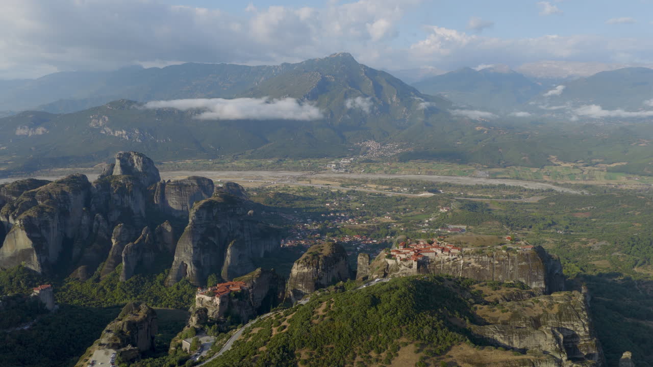 Cinematic aerial view of Meteora monastery in Greece perched on towering cliffs, dramatic rock formations and lush green valley create a breathtaking historic scene