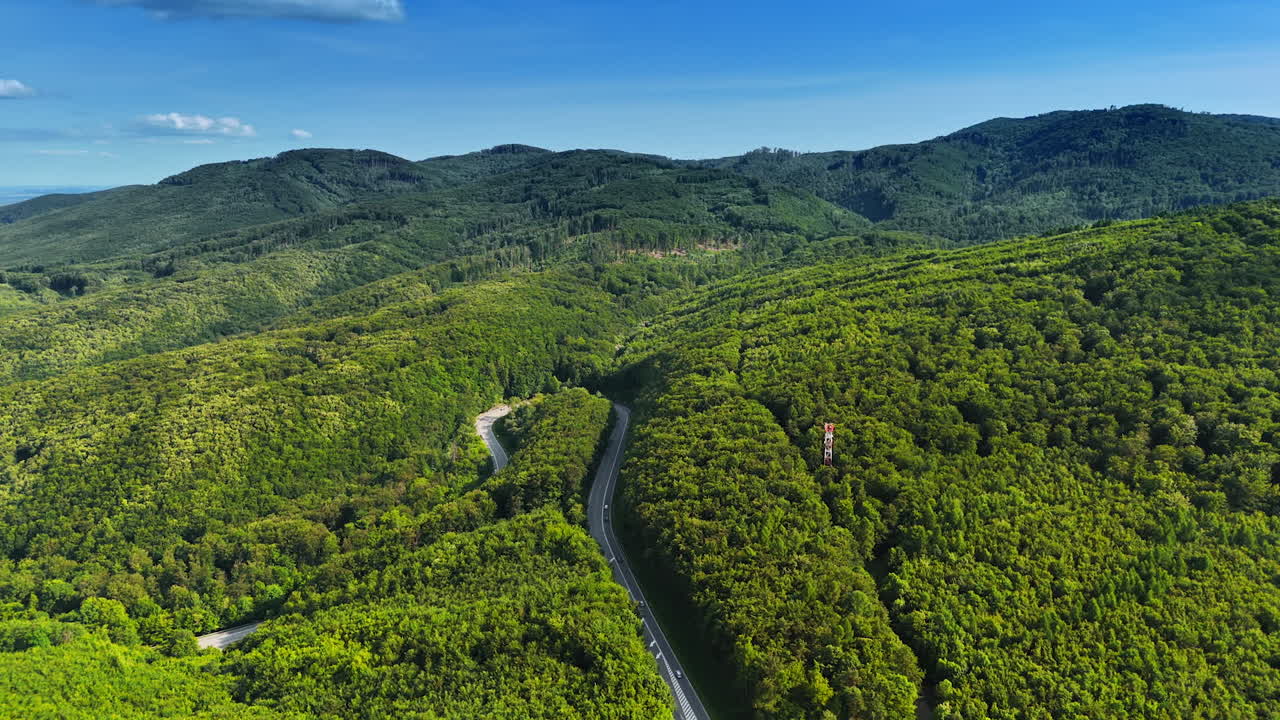 Green fields under blue skies. Aerial view reveals a vibrant green landscape with winding roads among hills and dense forests on a sunny day
