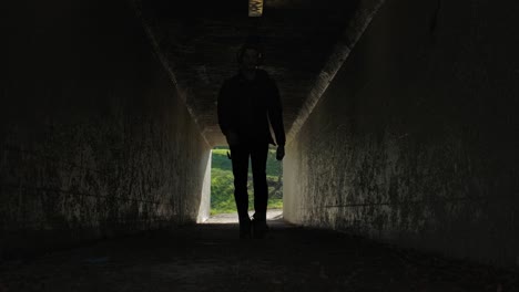 silhouetted figure walks through tunnel, bright daylight visible outside, conveying hope, mystery