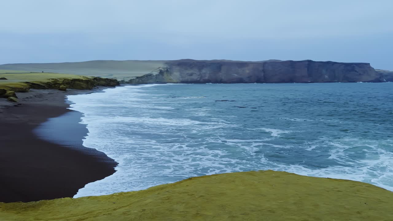 Tide recedes over rocks on Playa de Rojas coast, exposing black sand and wet surfaces, slow motion establishing pan right