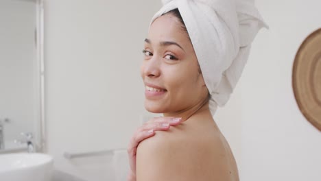 portrait of biracial woman with towel smiling in bathroom