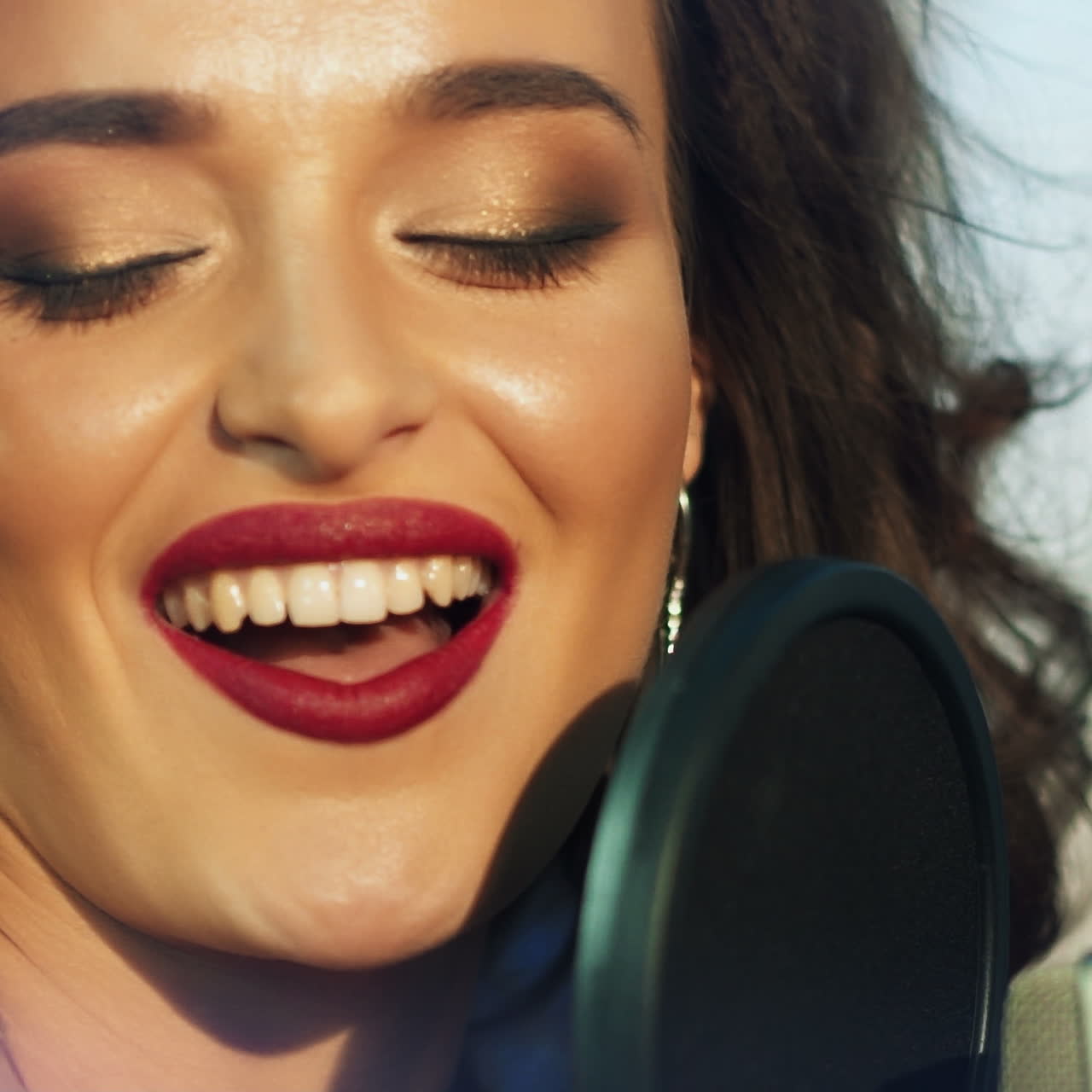 Sexy female with a happy face singing in the professional mic and looking at camera. Beautiful singer performing a song into the microphone in studio. Slow motion. Close-up
