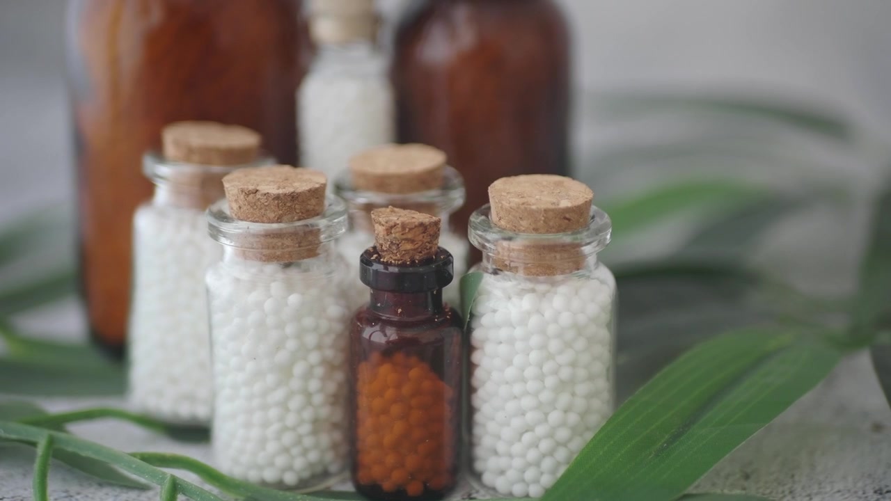 Kleine Glasflaschen gefüllt mit homöopathischen Pillen auf einem grünen Blatt