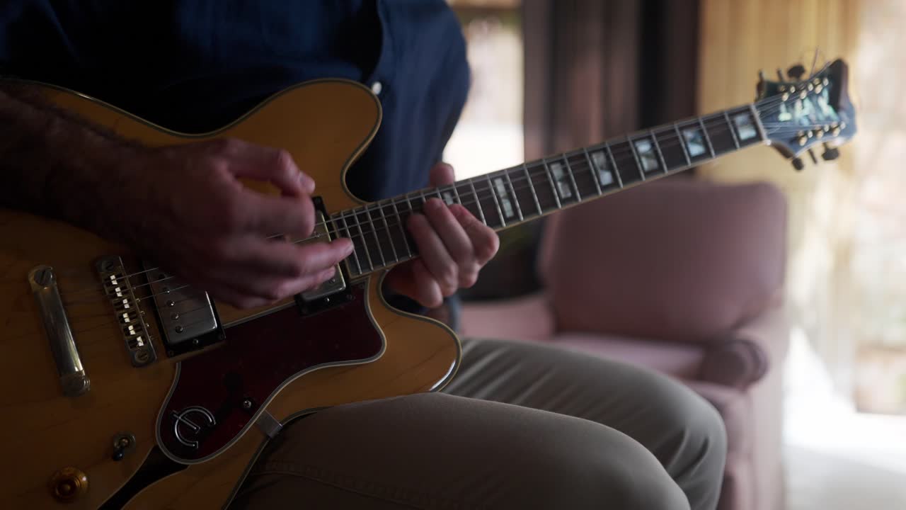Close up view of a man playing an electric guitar in a home studio.