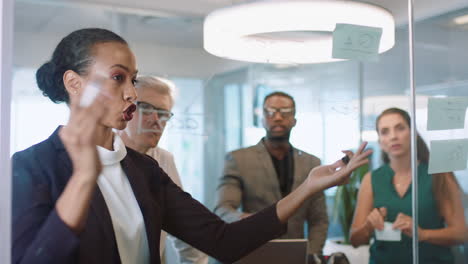 Geschäftsleute,-Die-Haftnotizen-Verwenden,-Brainstorming,-Teamleiterin,-Frau,-Die-Mit-Kollegen-Arbeitet-Und-Auf-Einem-Glas-Whiteboard-Schreibt,-Das-Problemlösungsstrategien-Bei-Bürobesprechungen-Durch-Glas-Zeigt