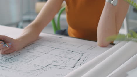 Close-Up-Of-Female-Architect-In-Office-Working-At-Desk-Making-Notes-On-Plan-Or-Blueprint