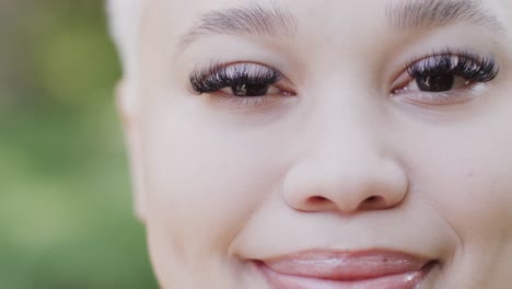 Portrait-of-happy-biracial-woman-in-garden-with-big-green-leaves-in-slow-motion