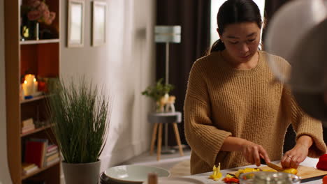 woman at home in kitchen preparing healthy fresh vegetables for vegetarian or vegan meal slicing yellow pepper on board