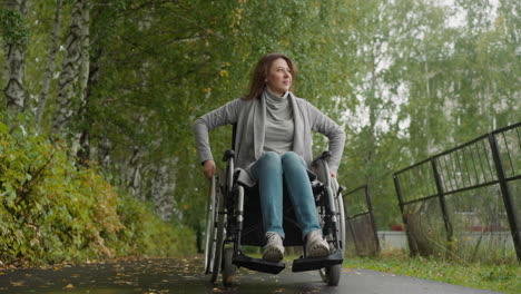 woman with injury moves turning wheels of wheelchair in park