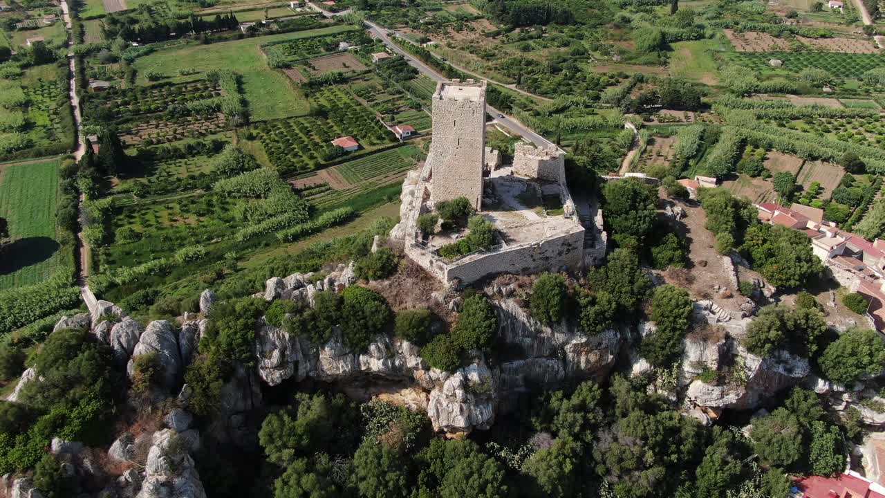 This is a zoom out video that shows luscious green fields and vineyards near a castle. The video pans right showing the deep blue water coastline
