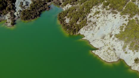 Lago-Tranquilo-Con-Agua-Verde-Que-Lava-La-Hermosa-Costa-De-Montañas-Alpinas-Con-Vegetación-Exuberante,-Vista-Aérea