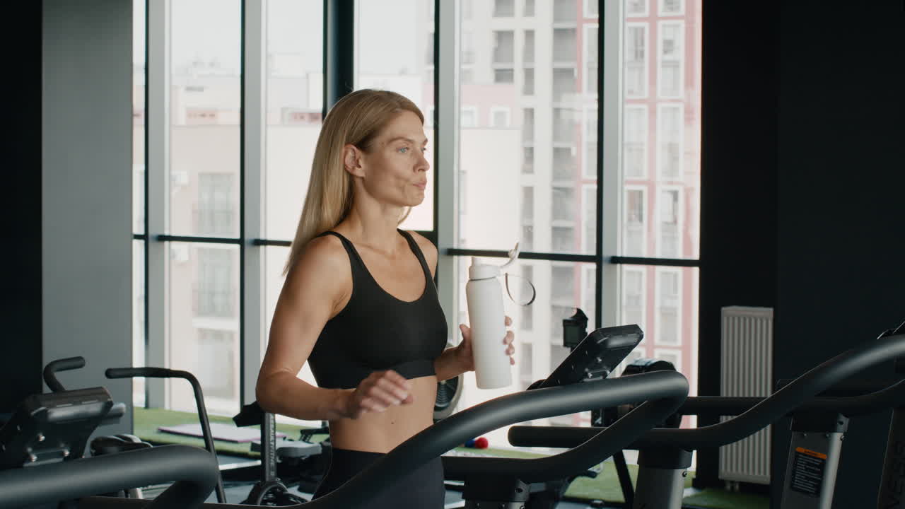 Woman drinking water on a treadmill at the gym