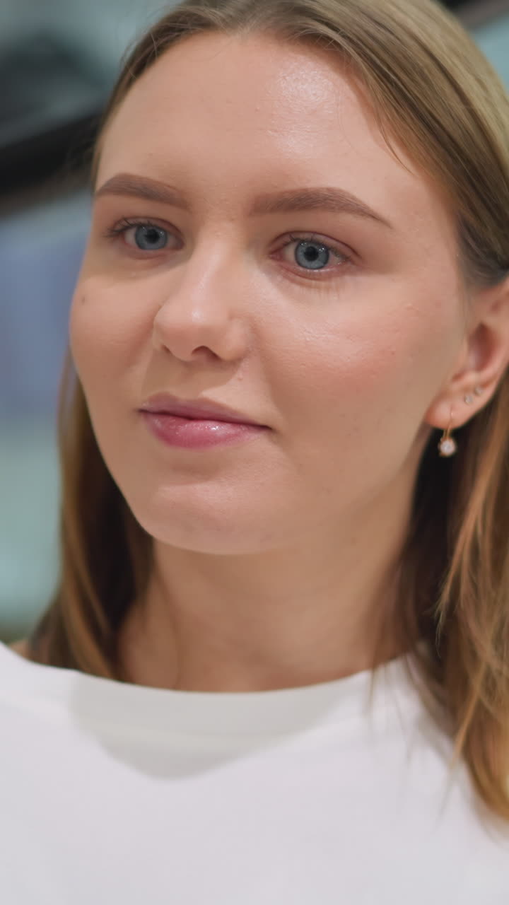 dama contemplativa sentada en un moderno centro comercial con una sonrisa sutil, vestida con una camiseta blanca y rodeada de un ambiente elegante, el fondo elegante presenta exhibiciones minoristas y escaleras mecánicas de vidrio