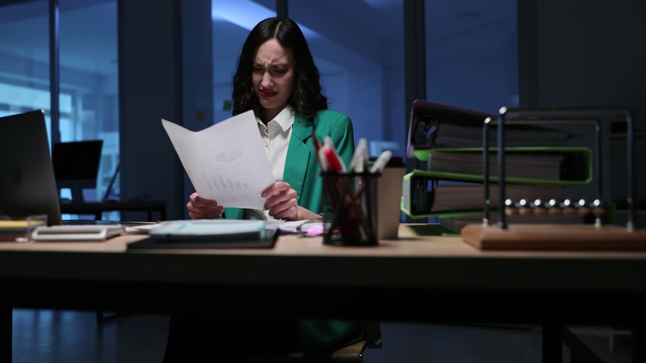 Funcionária de escritório descontente lê documento perto do laptop altas horas da noite