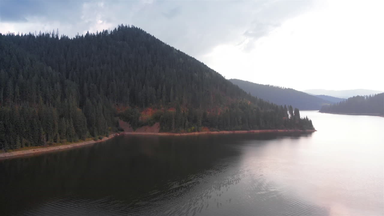 Aerial Footage of Large Lake and mountains surrounded by Pine Forest trees
