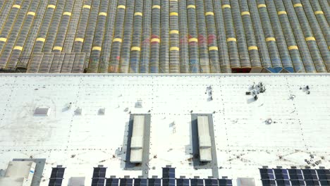 Aerial View of Solar Panels on a Large Industrial Rooftop Adjacent to a Commercial Greenhouse
