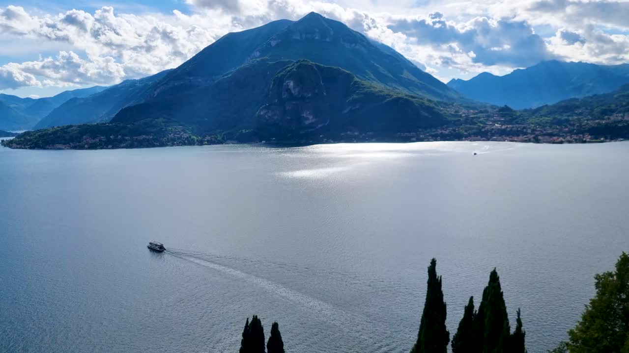 Panorama view from Varenna castle over lake Como in Italy and alpine mountains on a partly cloudy day. Ferry is crossing the lake.