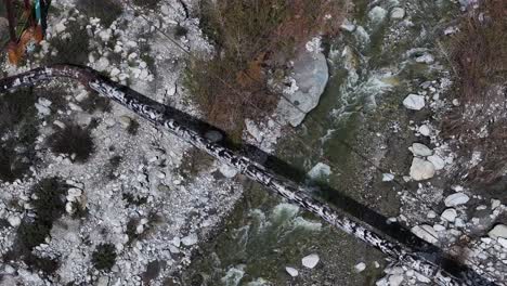 water pipeline in southern california passing over a rocky creek with fast-moving water aerial telephoto trucking pan 60fps slo mo