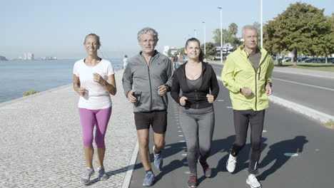 healthy group of mature people jogging on road near sea