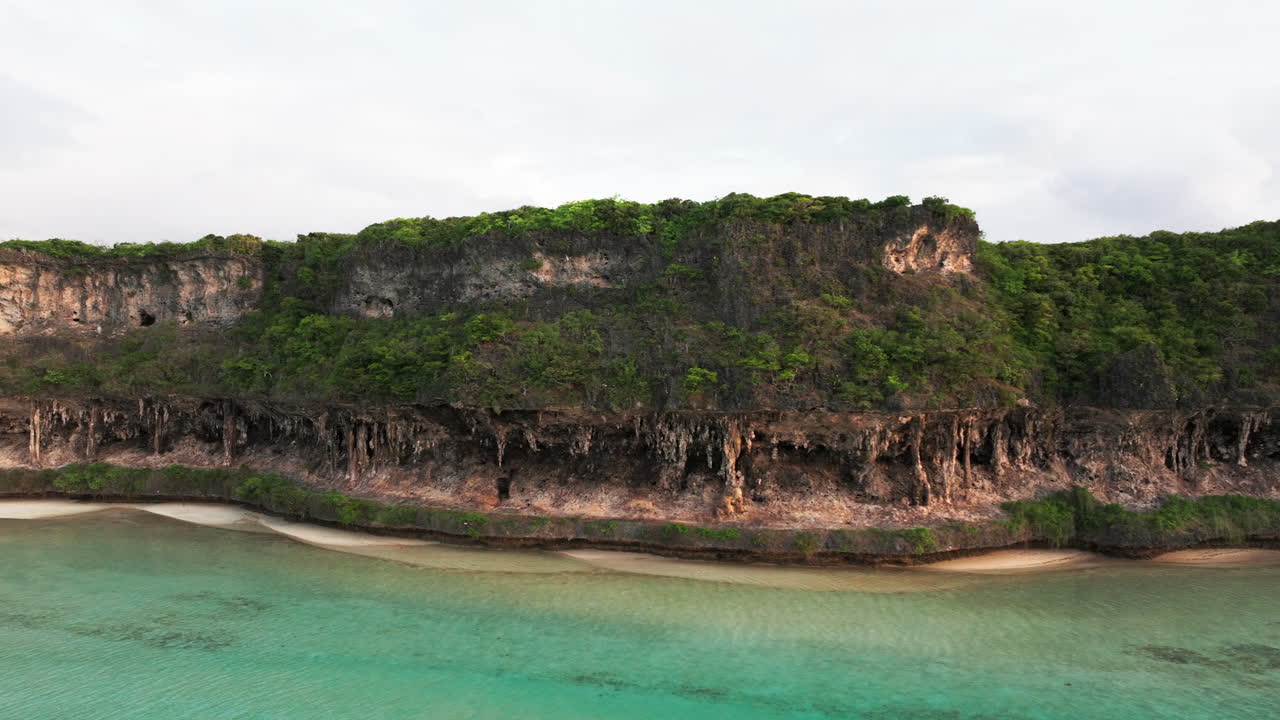 Drone footage of Lekini Bay cliffs and shallow turquoise waters in Ouvéa, New Caledonia, during soft evening light