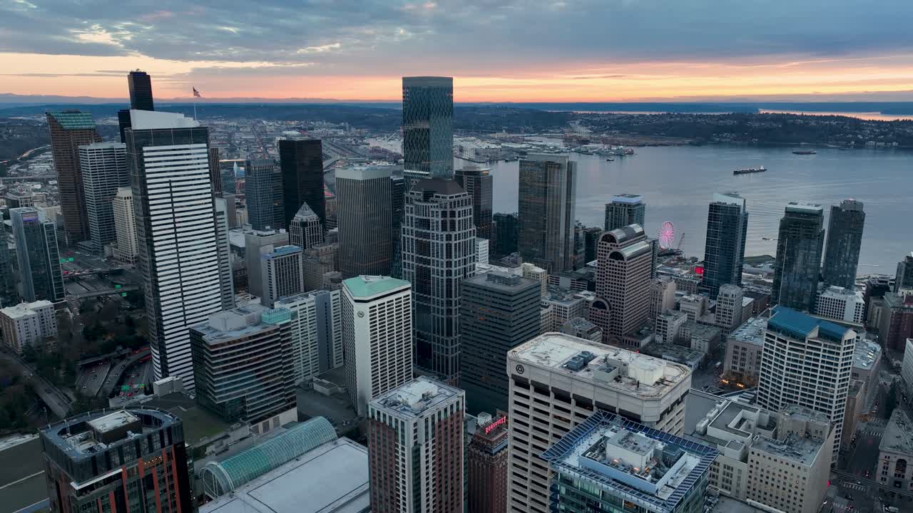 Aerial view of Seattle's downtown skyscrapers at sunset with a warm orange glow in the distance