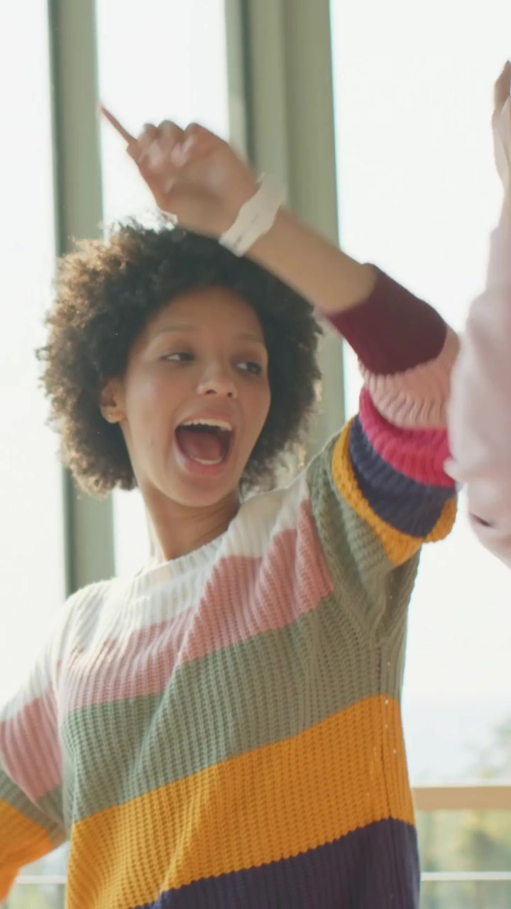 Vertical video: Smiling woman raising arm wearing watch in loft fist entering sparking playful bump