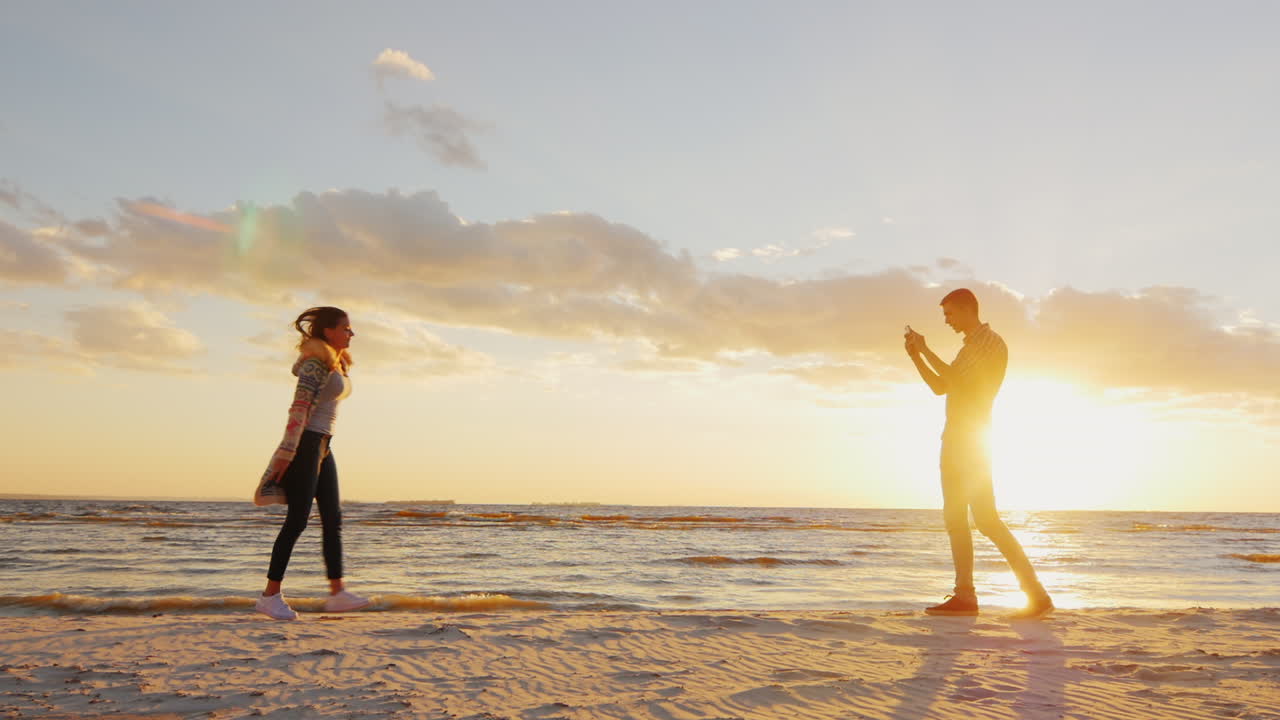 젊은 부부는 그의 여자 친구 전화 prores hq를 촬영하는 일몰 남자에 의해 바다에 의해 촬영됩니다