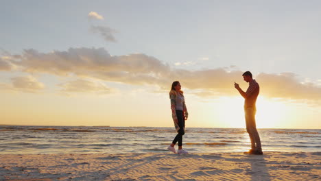 a young couple is photographed by the sea at sunset man photographing his girlfriend phone prores hq