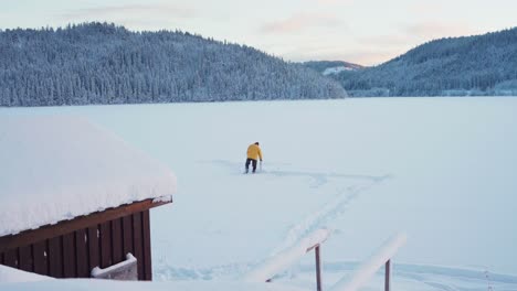 Panoramablick-Auf-Die-Winterlandschaft-Mit-Einem-Mann,-Der-Auf-Einem-Stuhl-Sitzt-Und-Im-Zugefrorenen-See-Fischt