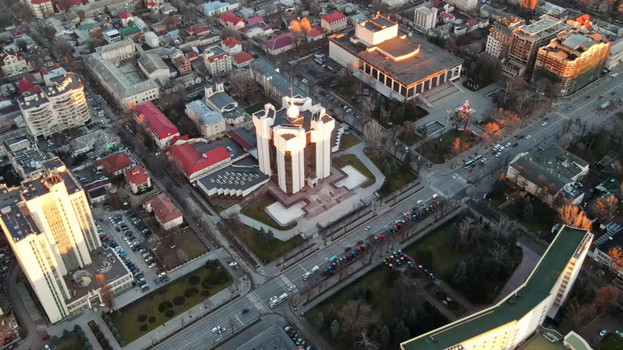 Aerial drone view of Chisinau at sunset. View of the Presidency and Parliament, multiple buildings in city center, roads with moving cars, bare trees. Moldova