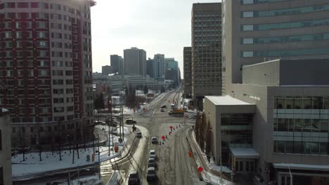 Aerial-forward-view-of-a-city-road-with-cars-parked-and-people-walking-by