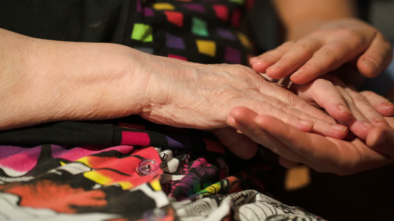 una joven acaricia las manos de su abuela.