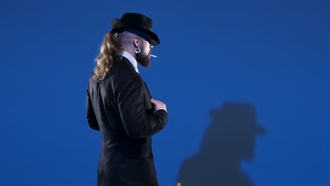 stylish man in suit and fedora smoking against blue background