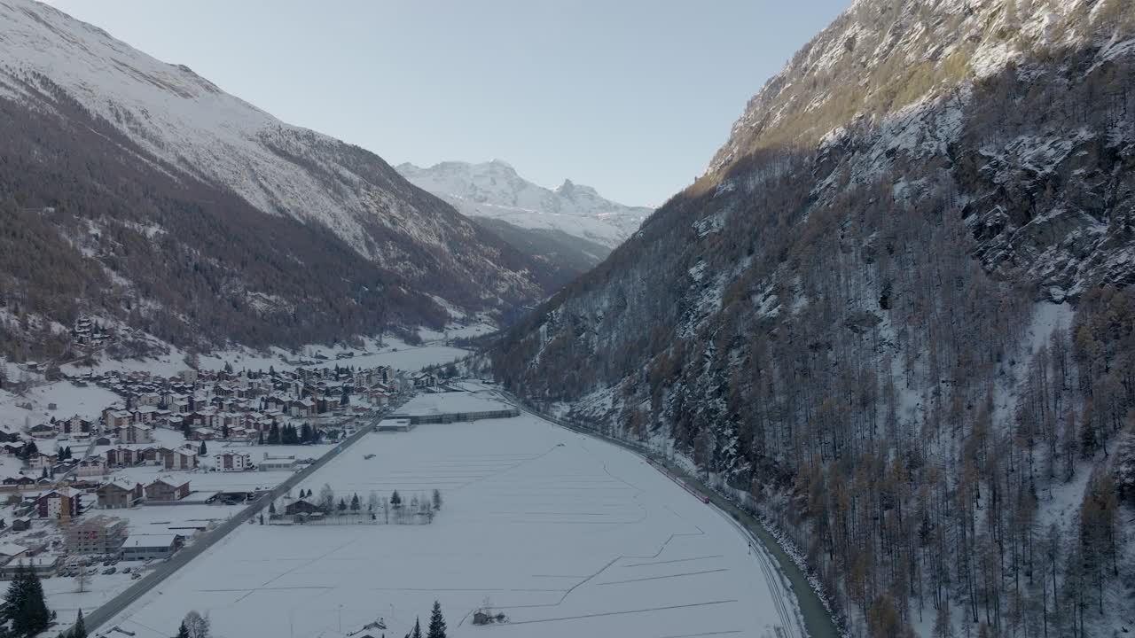 antena de drone lateral del tren rojo en suiza recorriendo un impresionante paisaje nevado de invierno junto al río que fluye con panorama de montañas alpinas