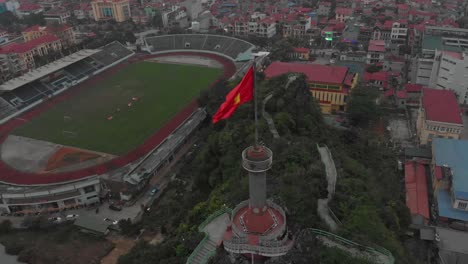 Flying-around-big-flagpole-at-Lang-son-Vietnam-during-cloudy-day,-aerial
