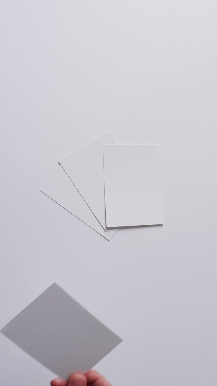 Vertical video of hand holding piece of paper over pieces of paper with copy space in slow motion