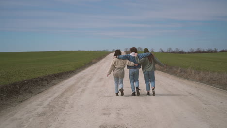 two young girls and a young boy walk backwards along a road in each other's arms