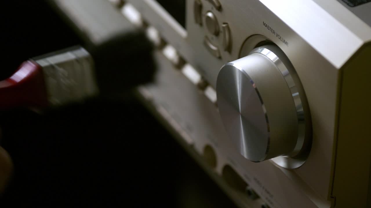 손은 방송 및 음악용 버튼이 있는 홈 시어터 시스템에서 증폭기의 먼지 브러시를 사용하고 있습니다.