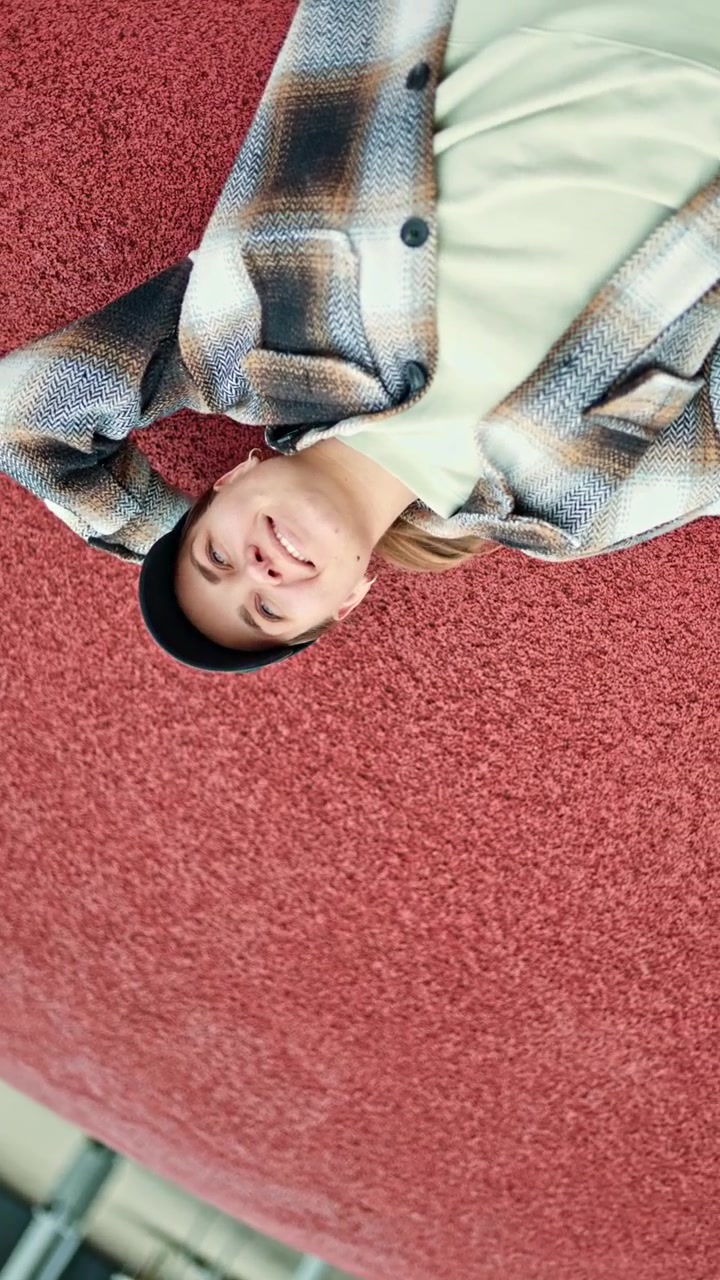 Young person lying on red surface, looking up with relaxed expression, in a casual outfit during daytime, showcasing a unique perspective and playing with angles