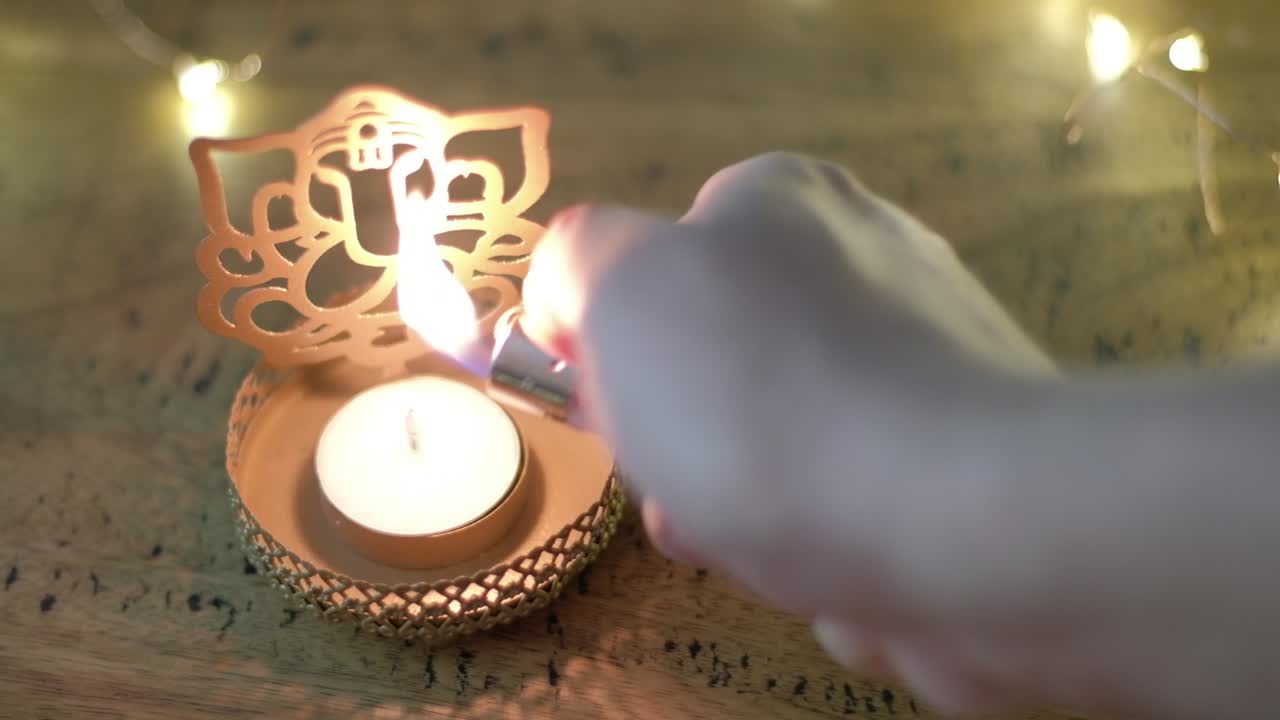Closeup of a man's hand lighting a golden tea light holder cutout of Hindu God Ganesha to worship  during the festival of lights or Diwali or Deepawali