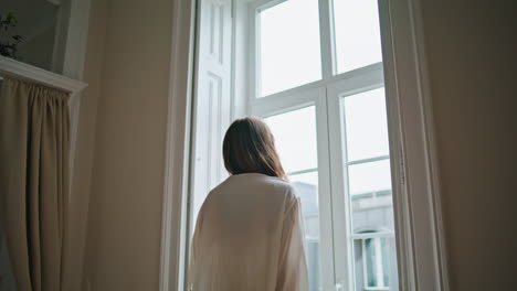 una mujer joven mirando la ventana de su casa por la mañana de cerca. una chica relajada disfrutando del fin de semana.