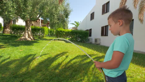 niño participando en las tareas domésticas y regando el césped verde de la casa