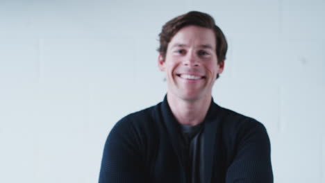 Portrait-Of-Smiling-Man-Wearing-T-Shirt-Walking-Into-Focus-Against-White-Studio-Wall