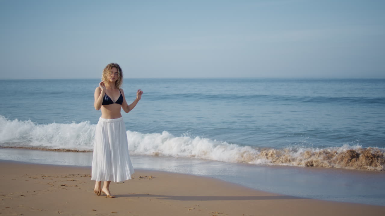 танцовщица поднимает руки, гуляет по летнему пляжу.
